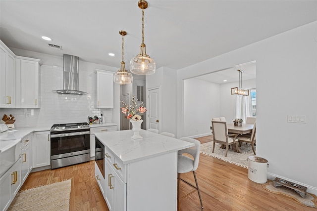 kitchen featuring visible vents, a breakfast bar, light wood-style flooring, stainless steel range, and wall chimney exhaust hood