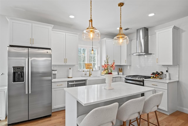 kitchen featuring appliances with stainless steel finishes, light wood-style floors, wall chimney range hood, and a sink