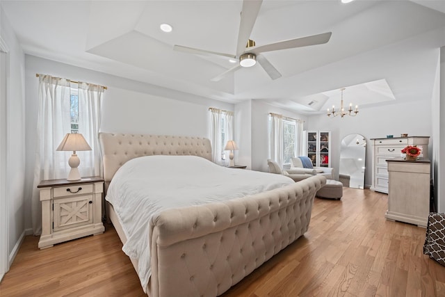 bedroom featuring light wood finished floors, ceiling fan with notable chandelier, baseboards, and a tray ceiling