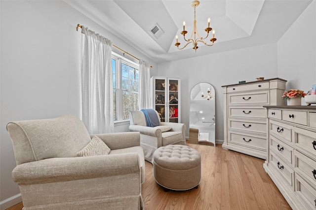 sitting room with visible vents, an inviting chandelier, a tray ceiling, vaulted ceiling, and light wood-style floors