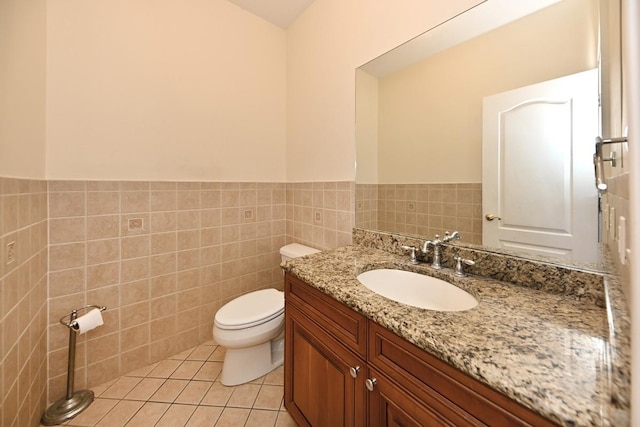 half bath with vanity, tile walls, toilet, a wainscoted wall, and tile patterned floors