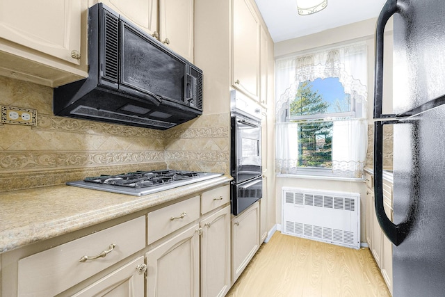 kitchen featuring radiator, oven, freestanding refrigerator, gas cooktop, and a warming drawer