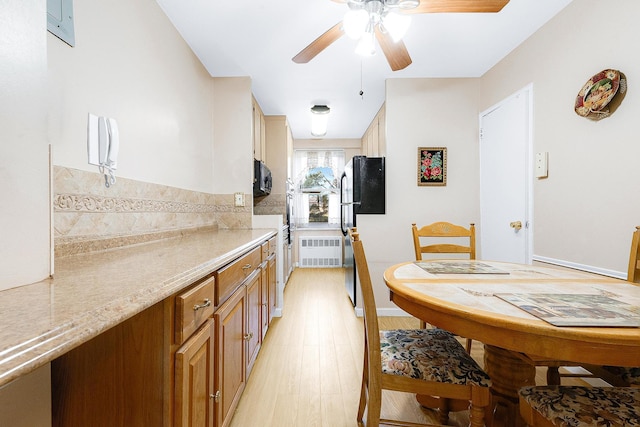 kitchen with radiator, light wood-style flooring, freestanding refrigerator, ceiling fan, and black microwave