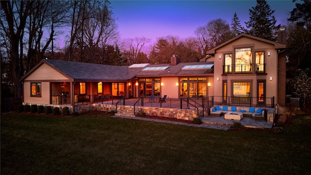 30 Half Moon Ln, Irvington, NY 10533 - back of house at dusk with an outdoor hangout area, roof mounted solar panels, a balcony, a lawn, and a patio