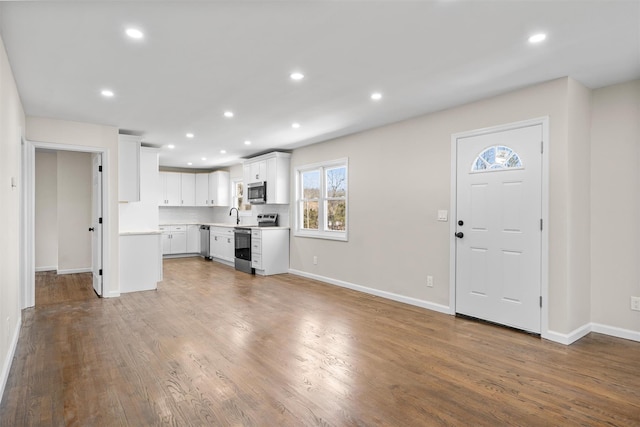 unfurnished living room with recessed lighting, baseboards, wood finished floors, and a sink