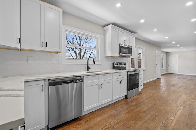 kitchen with wood finished floors, a sink, stainless steel appliances, white cabinets, and backsplash