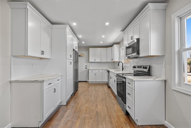 kitchen featuring backsplash, light wood-style flooring, stainless steel appliances, white cabinetry, and a sink