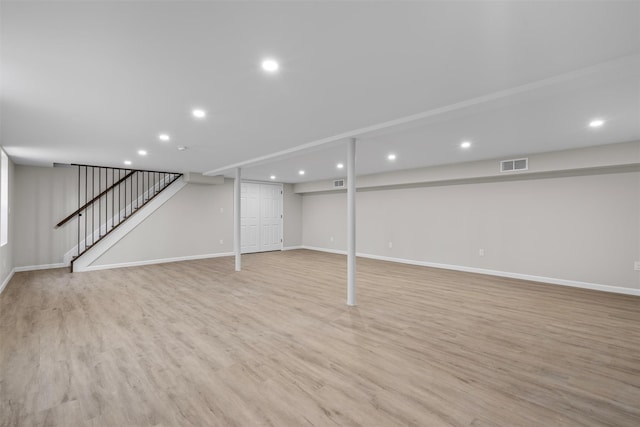 finished below grade area featuring visible vents, baseboards, light wood-style floors, and stairway