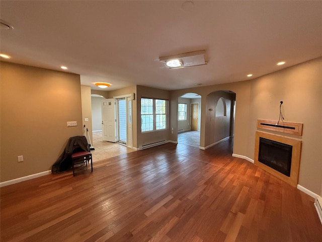 unfurnished living room with wood finished floors, a baseboard heating unit, arched walkways, and a glass covered fireplace