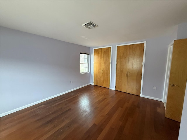 unfurnished bedroom featuring visible vents, baseboards, dark wood-type flooring, and multiple closets