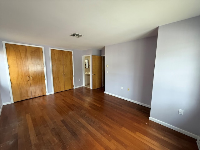 unfurnished bedroom featuring dark wood-type flooring, baseboards, visible vents, and multiple closets