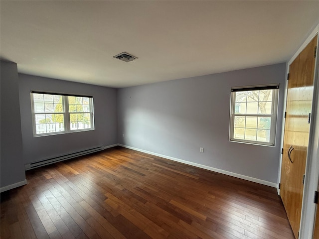 empty room featuring dark wood finished floors, baseboard heating, visible vents, and baseboards