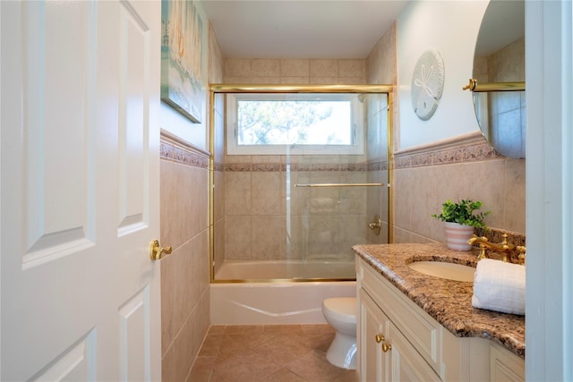 bathroom with toilet, combined bath / shower with glass door, tile walls, tile patterned flooring, and vanity