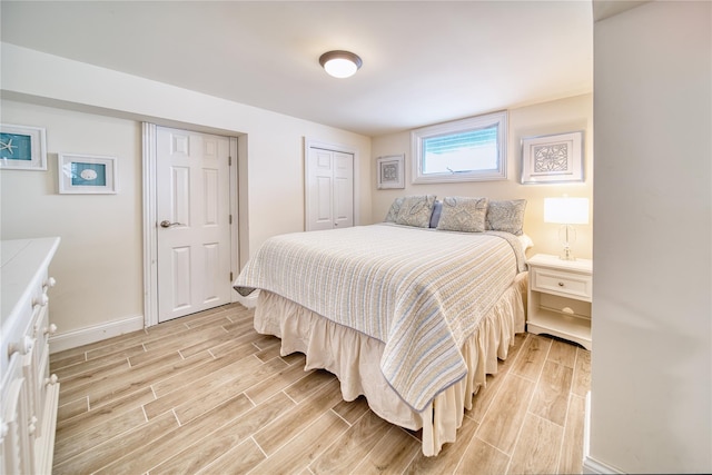 bedroom with baseboards, multiple closets, and wood finish floors