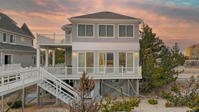 back of property at dusk featuring stairway, a balcony, and roof with shingles