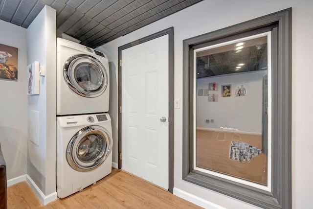 laundry area with laundry area, stacked washing maching and dryer, light wood-type flooring, and baseboards