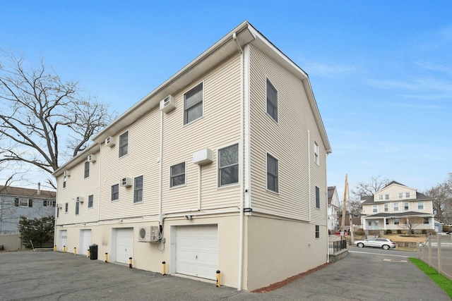 back of house featuring a residential view, an AC wall unit, a wall unit AC, driveway, and an attached garage