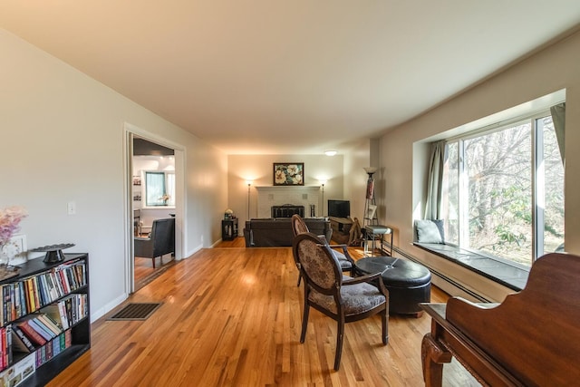 living room with a brick fireplace, light wood-style flooring, visible vents, and baseboards