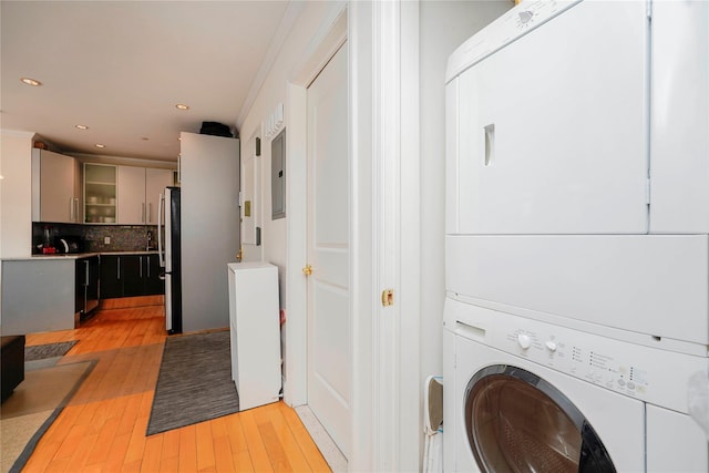 laundry area featuring electric panel, recessed lighting, light wood-style floors, stacked washer / dryer, and laundry area