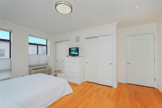 bedroom with a wall mounted air conditioner, multiple closets, light wood-style flooring, ornamental molding, and baseboards