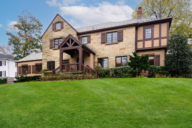 tudor-style house featuring stone siding, stucco siding, a chimney, and a front lawn