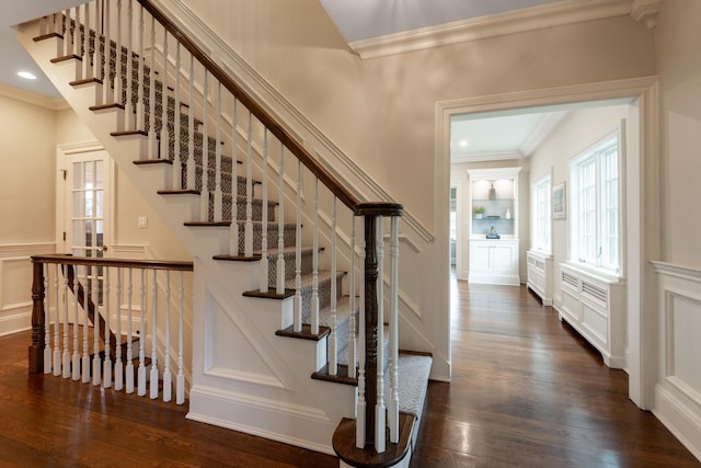 stairway with wood finished floors, a wainscoted wall, recessed lighting, ornamental molding, and a decorative wall