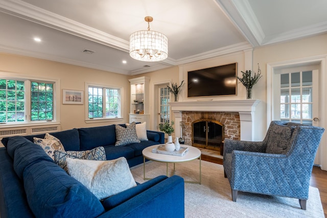 living room with a chandelier, a stone fireplace, wood finished floors, and crown molding