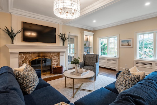 living area with ornamental molding, recessed lighting, wood finished floors, a notable chandelier, and a glass covered fireplace