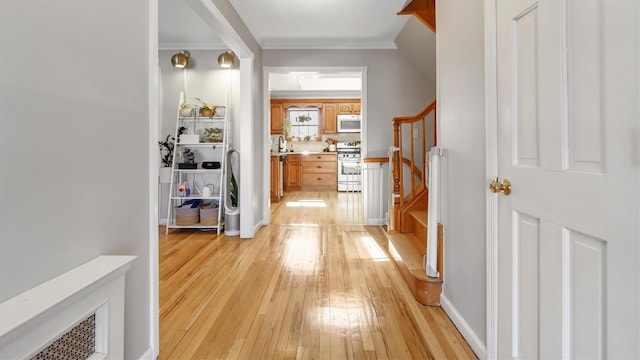 hallway featuring baseboards, stairs, ornamental molding, light wood-style floors, and a sink