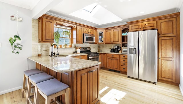 kitchen with a sink, stainless steel appliances, a peninsula, a skylight, and brown cabinetry