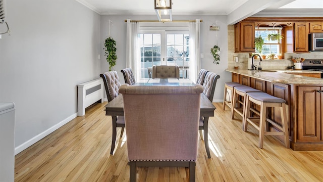 dining room featuring light wood-style flooring, radiator heating unit, baseboards, and ornamental molding