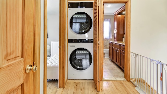 laundry area with stacked washer / dryer, light wood-style flooring, and laundry area