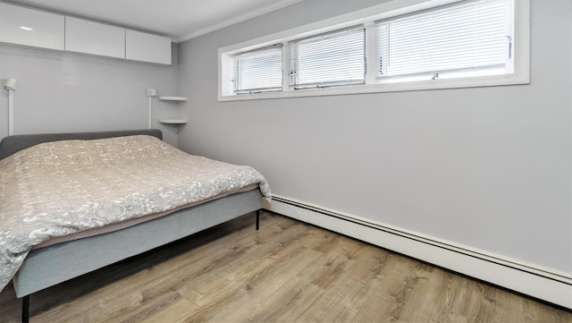 bedroom with a baseboard heating unit, wood finished floors, and crown molding