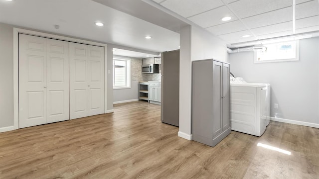 laundry area with washing machine and dryer, baseboards, and light wood-style floors