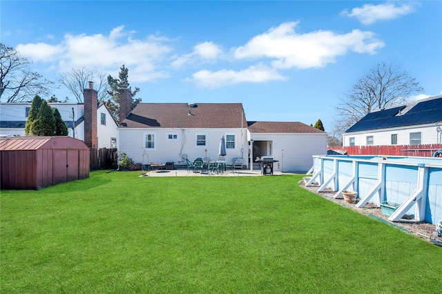 rear view of house with an outbuilding, a fenced in pool, fence, a yard, and a storage shed