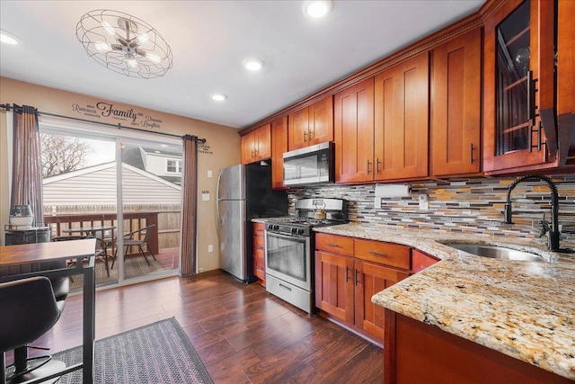 kitchen with glass insert cabinets, light stone countertops, brown cabinets, stainless steel appliances, and a sink