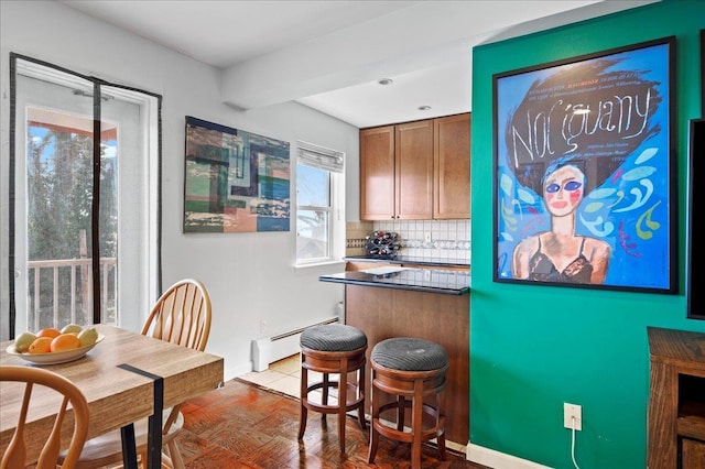 kitchen featuring dark countertops, baseboard heating, backsplash, and a breakfast bar