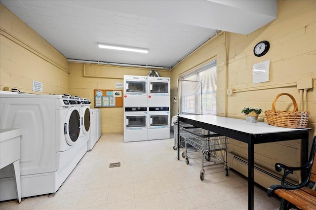 common laundry area featuring independent washer and dryer, light floors, stacked washer / drying machine, and concrete block wall