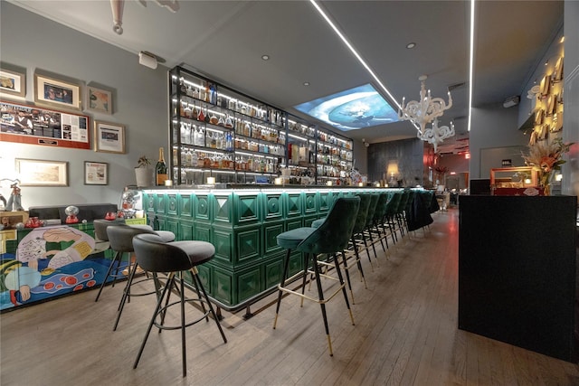 bar with a bar, an inviting chandelier, and hardwood / wood-style floors