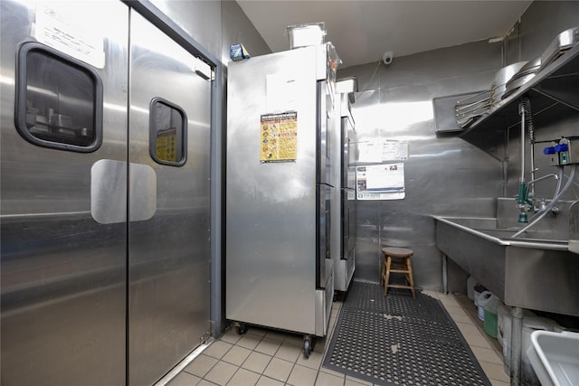 kitchen featuring light tile patterned floors, stainless steel refrigerator, freestanding refrigerator, and a sink