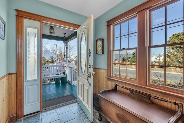 doorway to outside featuring stone tile floors, wood walls, wainscoting, and a healthy amount of sunlight