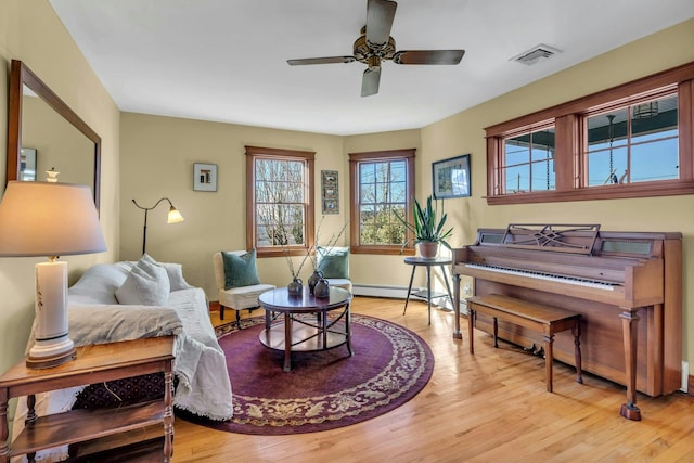 sitting room featuring visible vents, baseboard heating, wood finished floors, and a ceiling fan