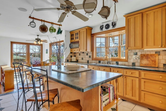 kitchen featuring light tile patterned flooring, a sink, dark countertops, a kitchen breakfast bar, and tasteful backsplash