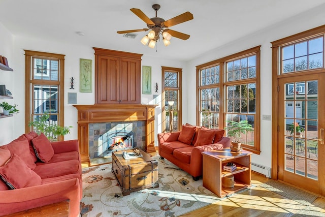 living area with visible vents, wood finished floors, baseboard heating, ceiling fan, and a tile fireplace