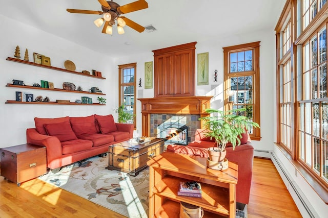 living area featuring light wood finished floors, visible vents, a tiled fireplace, baseboard heating, and a ceiling fan