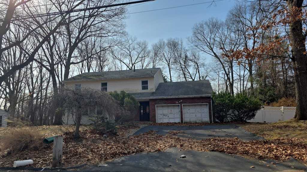 view of front of home with brick siding, an attached garage, driveway, and fence