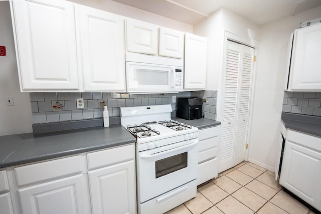 kitchen with white appliances, light tile patterned floors, white cabinets, dark countertops, and tasteful backsplash