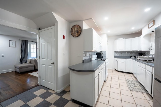 kitchen with dark countertops, backsplash, baseboards, white appliances, and white cabinetry