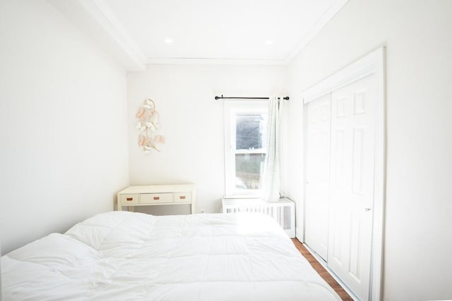 bedroom with radiator, wood finished floors, a closet, and ornamental molding