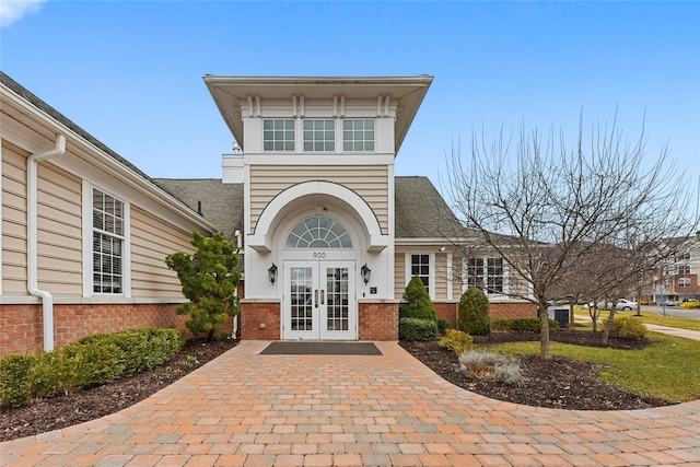 entrance to property with french doors, brick siding, and roof with shingles